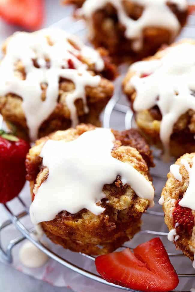 Strawberry Cinnamon Roll Muffins with a Cream Cheese Glaze on a cooling rack with fresh cut strawberries on the side. 