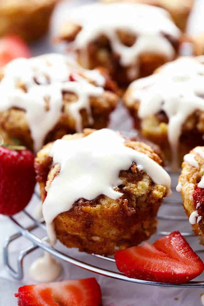 Strawberry Cinnamon Roll Muffins with a Cream Cheese Glaze on a cooling rack with fresh strawberries on the side. 
