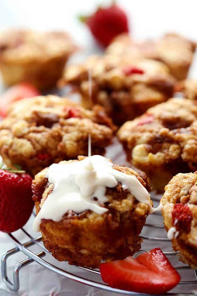 Strawberry Cinnamon Roll Muffins with a Cream Cheese Glaze on a cooling rack with sliced strawberries. 
