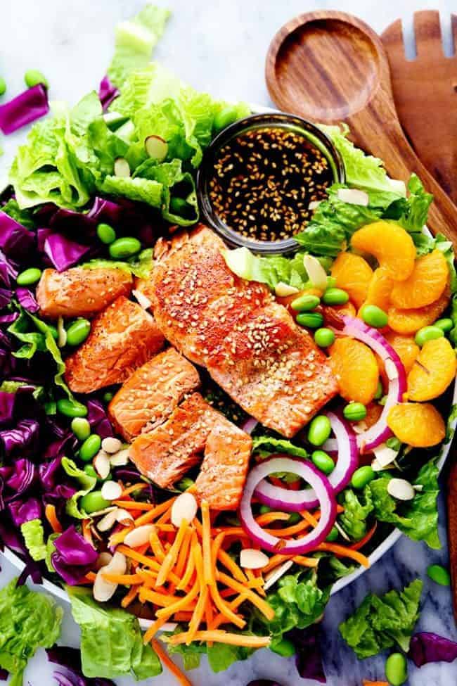 Overhead photo of Asian Pan Seared Salmon Salad in a large bowl with wooden tongs. 