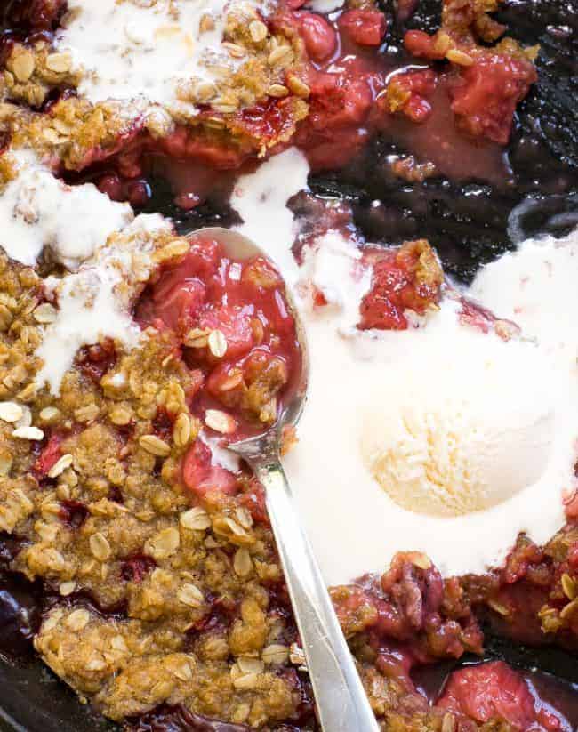 Strawberry Crisp in a bowl with a melting scoop of ice cream and a metal spoon. 