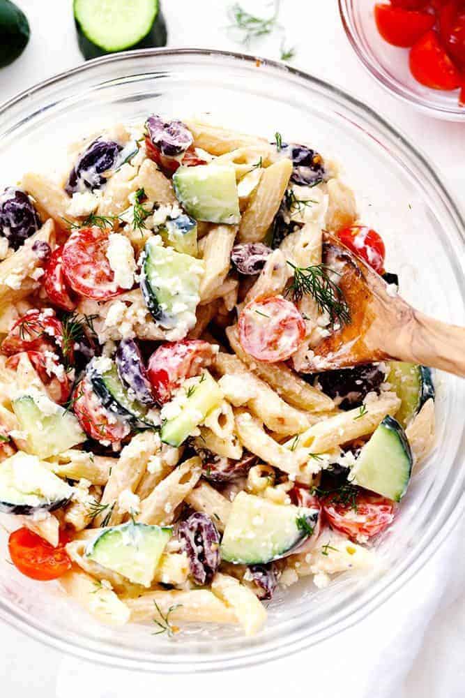 Greek Tzatziki Pasta Salad in a clear bowl with a wooden spoon. 