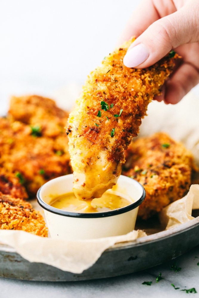 Chicken tender being dipped in a honey mustard sauce. 