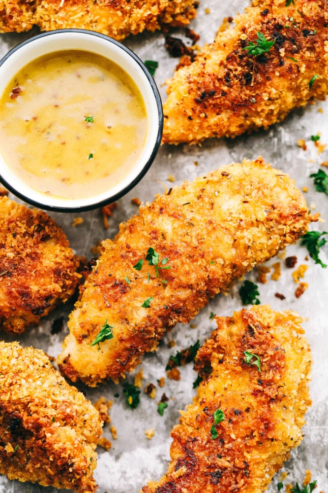 Chicken tenders on a baking sheet with honey mustard sauce. 
