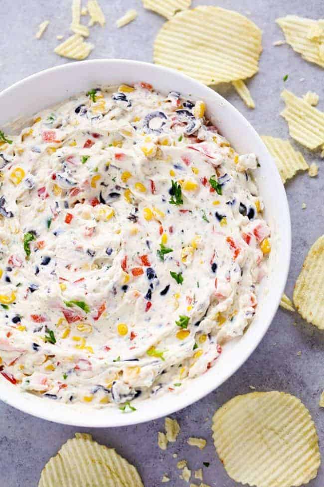 Loaded Creamy Ranch Dip in a white bowl with ruffled potato chips on the side. 