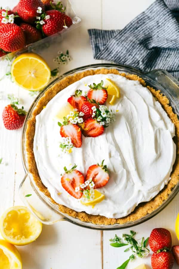 Lemon Pudding Pie in a clear pie pan with fresh strawberries and lemons on the side. 