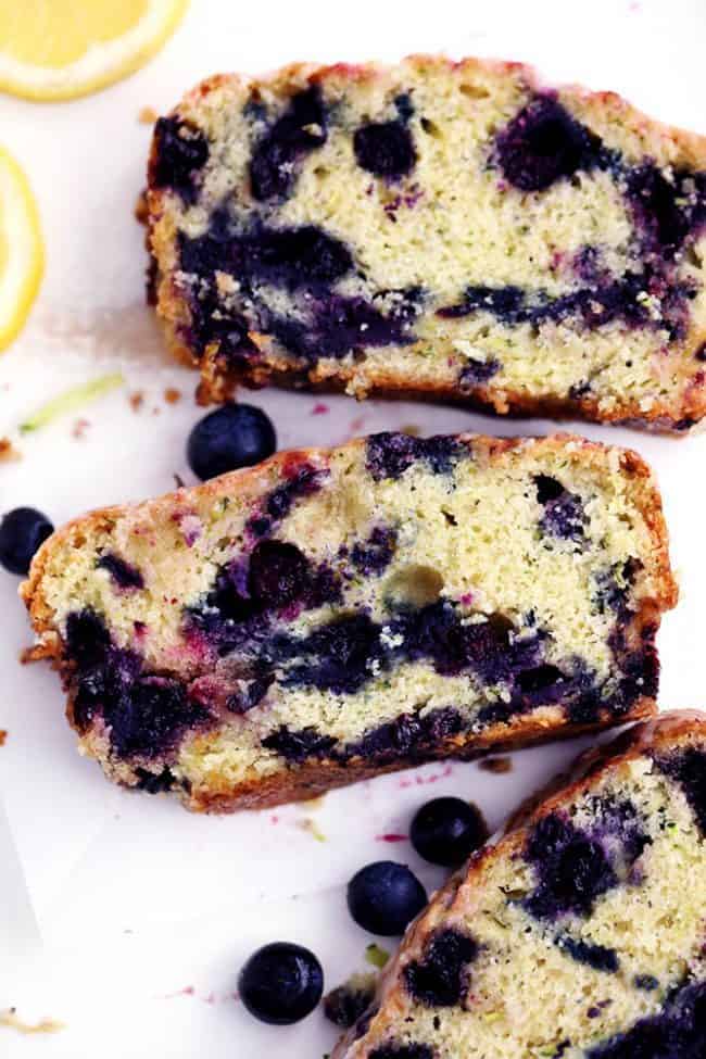 Blueberry Zucchini Bread with a Lemon Glaze that has been sliced and fresh blueberries next to it. 
