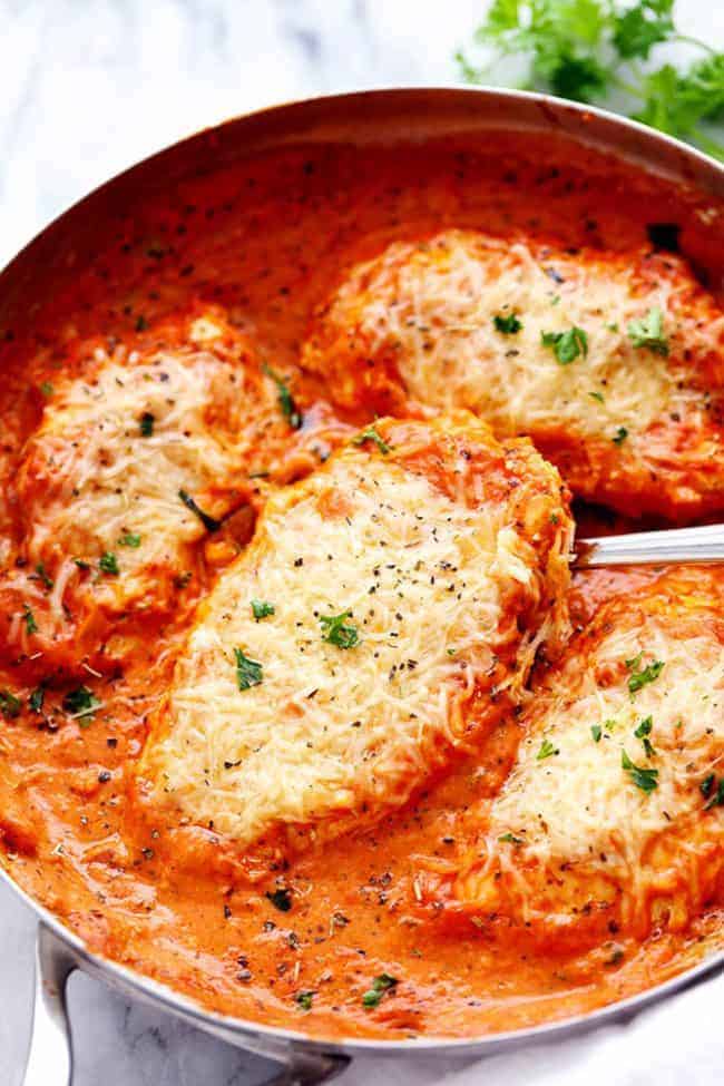 Overhead photo of Creamy Tomato Italian Parmesan Chicken in a large pan with a metal spoon. 