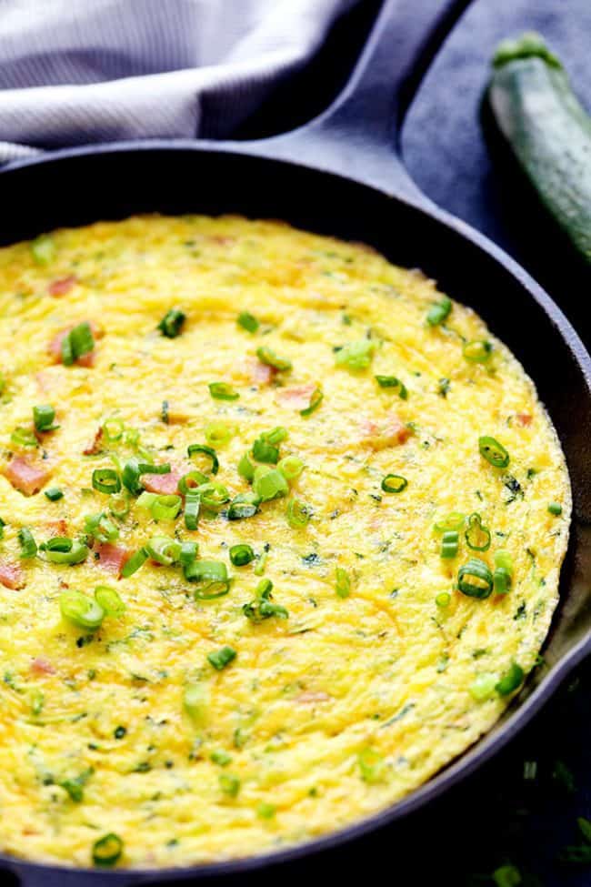 Ham and Cheddar Zucchini Frittata in a large pan with a Zucchini on the side. 