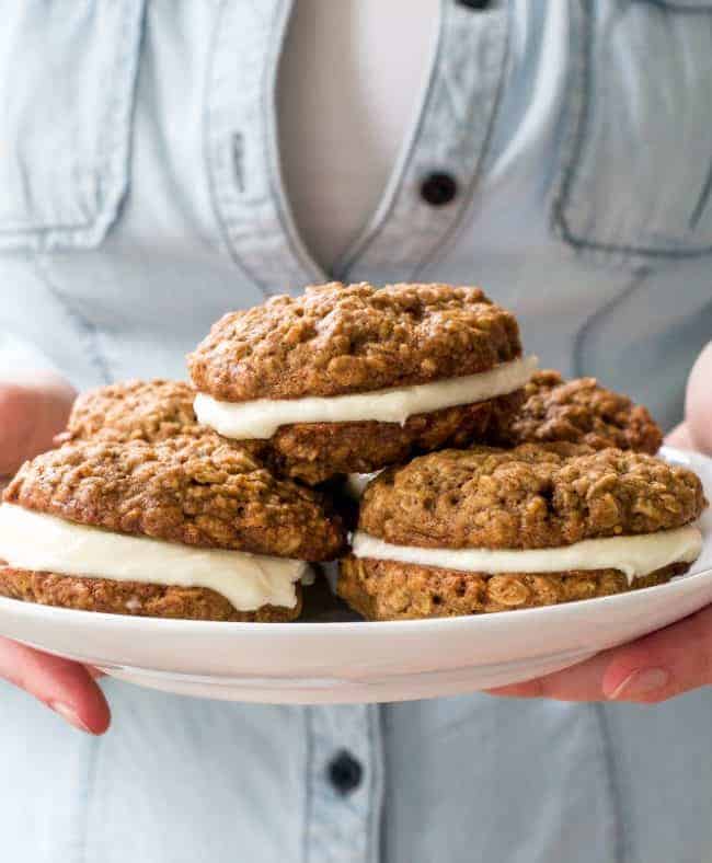 A person holding a white plate of Homemade Oatmeal Cream Pies stacked on one another. 