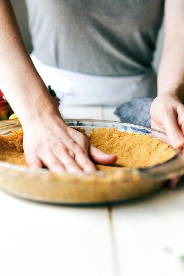 A hand pressing down the pie crust in the clear pie pan. 