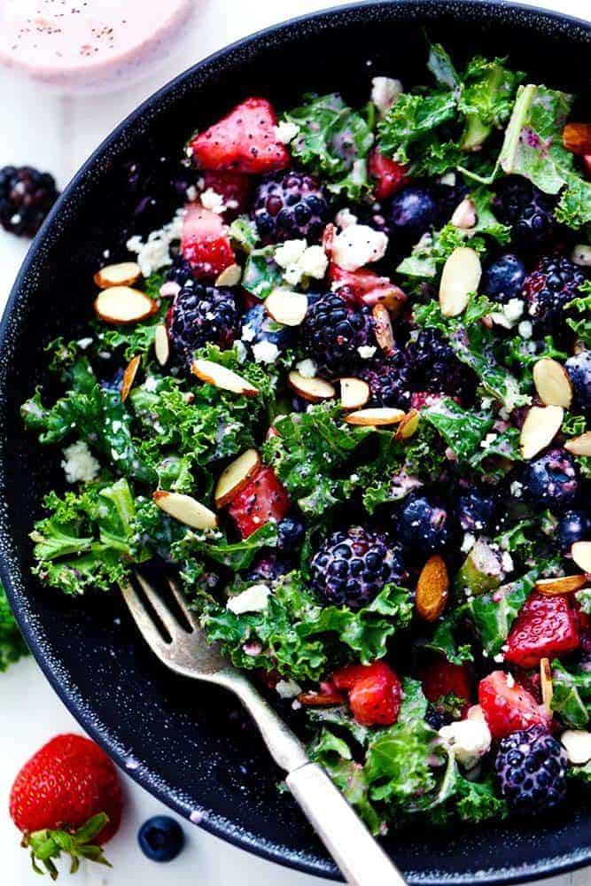 Triple Berry Kale Salad with Creamy Strawberry Poppyseed Dressing in a black bowl with a metal fork. 