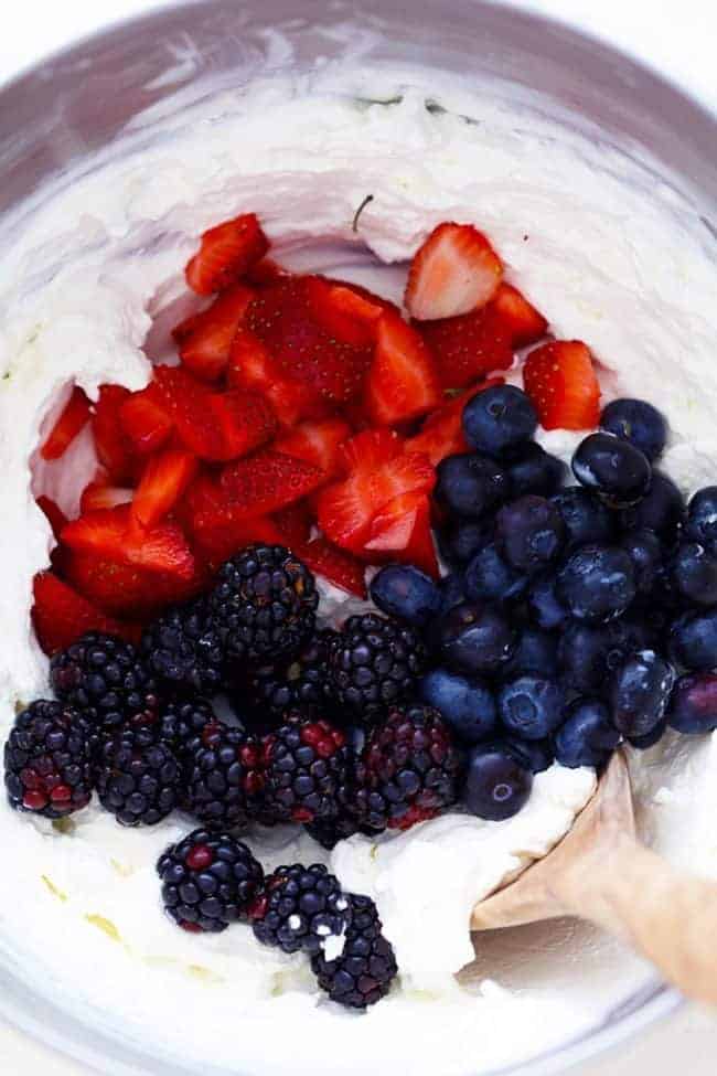 Strawberries, blackberries, and blueberries being mixed into the cheesecake mixture in a large mixing bowl. 