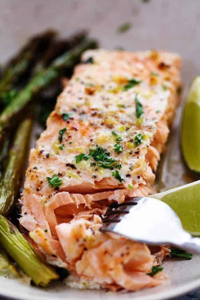 Buttery Garlic Lime Salmon with Asparagus on a white plate with a fork taking a bite size amount out. 
