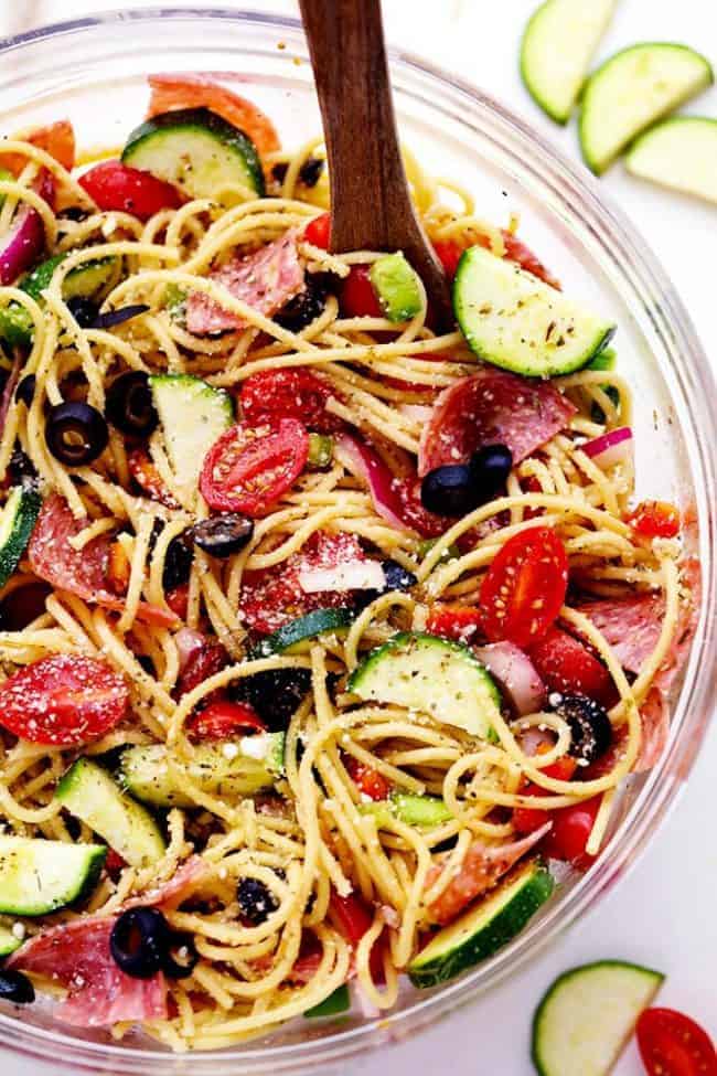 Italian Spaghetti Salad in a clear bowl with a wooden spoon. 