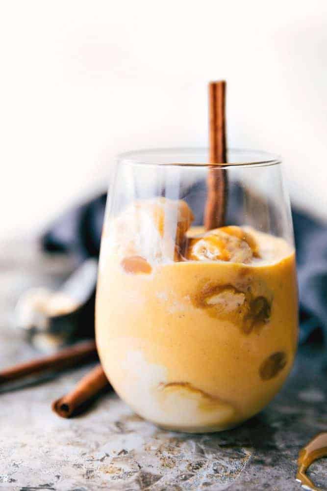 Pumpkin spice float in a clear glass with a cinnamon stick and ice cubes. 