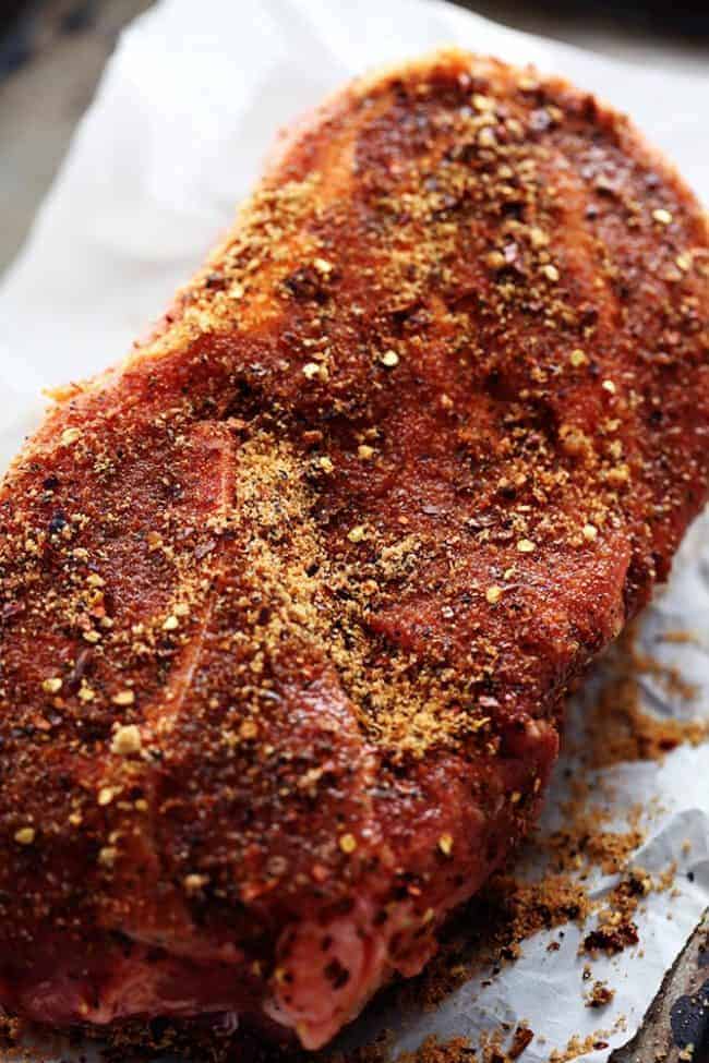 Pork slab on parchment paper with seasoning over top.