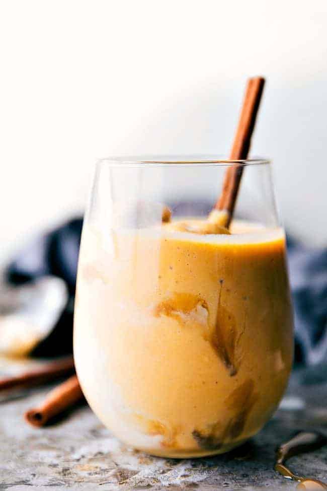 Pumpkin spice float in a clear glass with a cinnamon stick and ice cubes. 