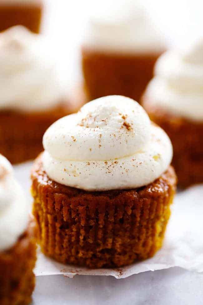 Pumpkin pie cupcakes with cream cheese whipping cream on a parchment paper.