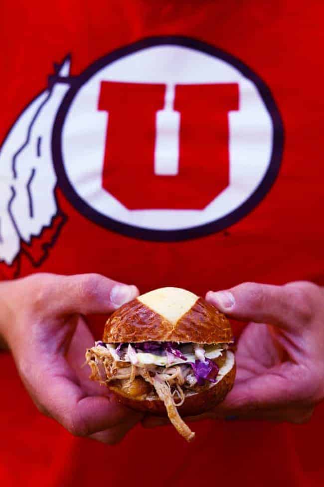 Slow cooker sweet Carolina pulled pork sliders being held by Remii Rivers in a university of Utah shirt.