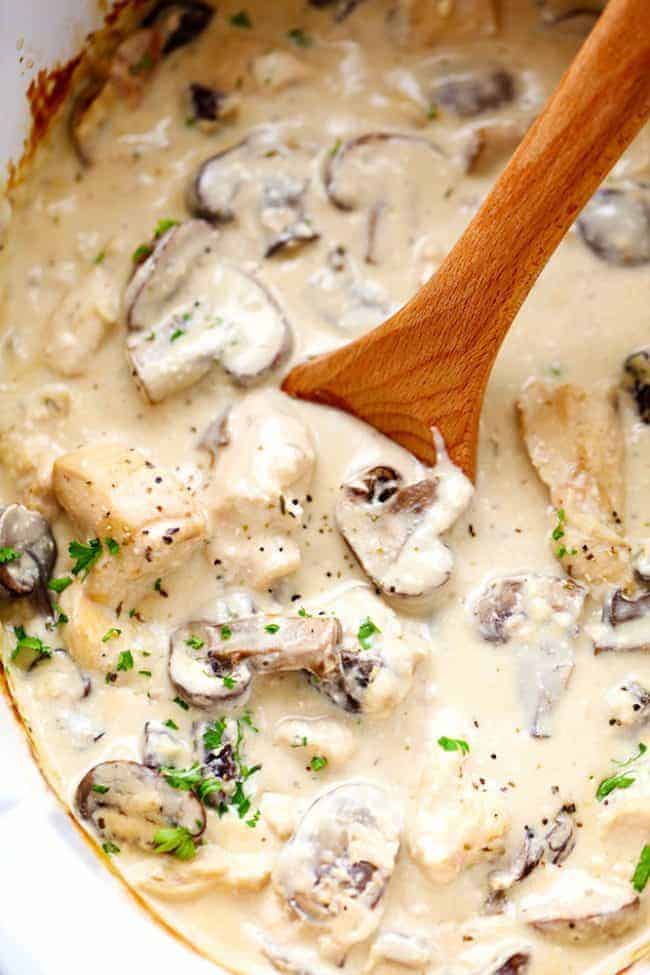 Chicken and mushroom stroganoff in a slow cooker with a wooden spoon stirring it. 