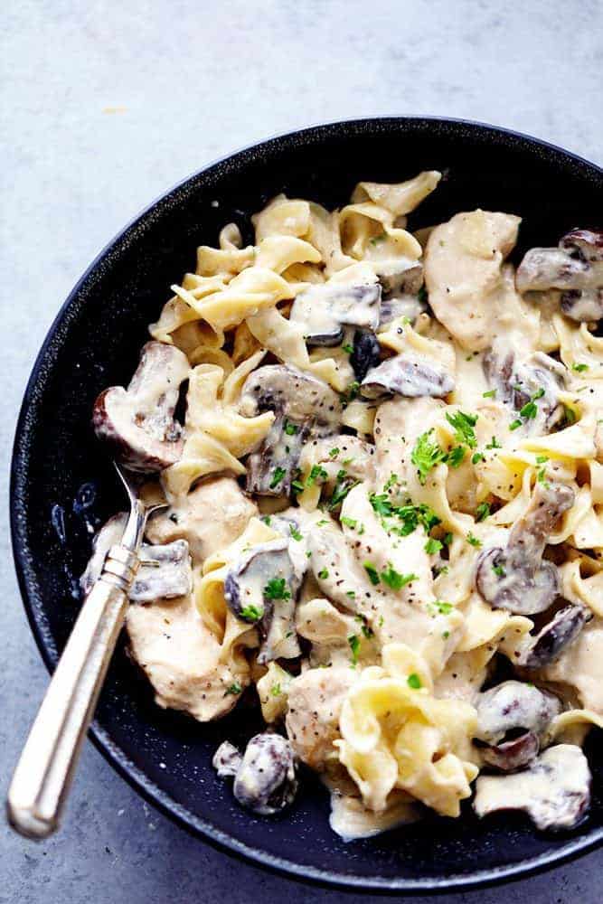 Slow cooker chicken and mushroom stroganoff in a black bowl with a fork on the side of the dish.