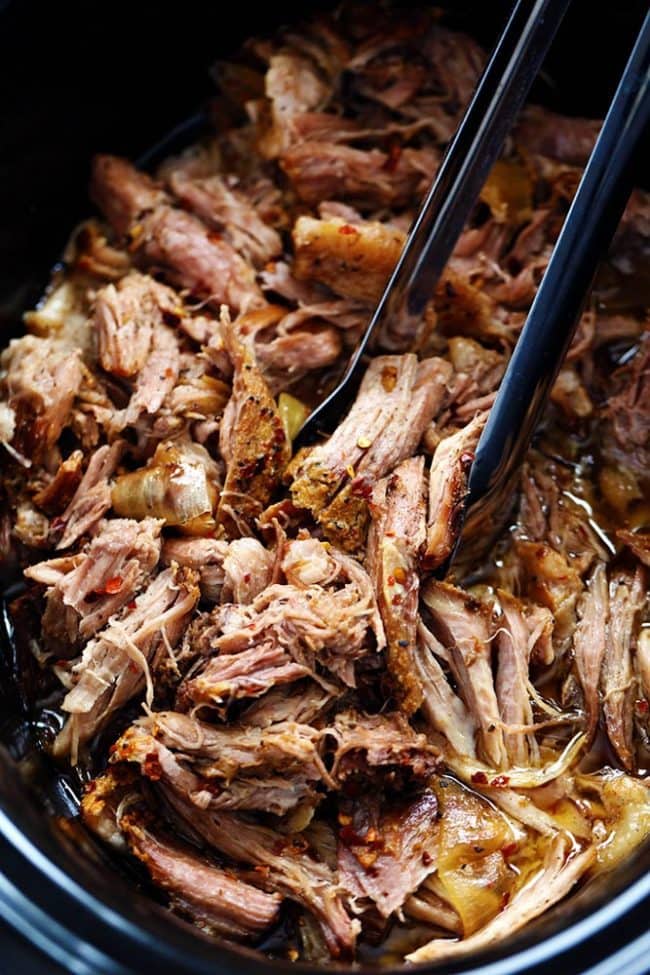 Slow cooker with sweet Carolina pulled pork in it being stirred with black tongs.