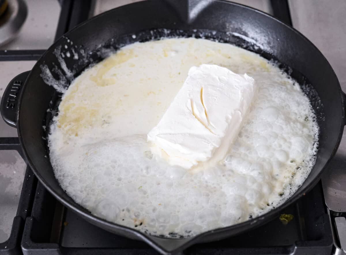 Angle s hot of butter, garlic, cream cheese, and heavy cream melting in a skillet. 