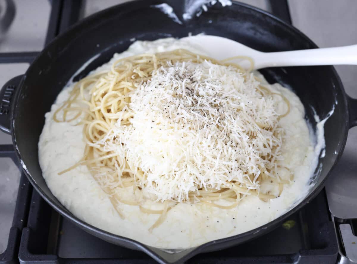 Overhead shot of the noodles, parmesan cheese, salt and pepper added to the cream cheese and heavy cream mixture. 