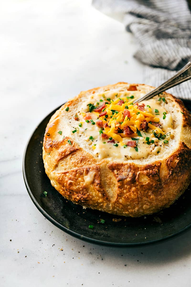 Red potato soup in a bread bowl with a spoon in the soup. 