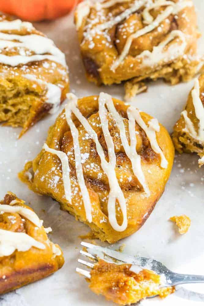 Pumpkin cinnamon rolls with frosting on white granite counter top. 
