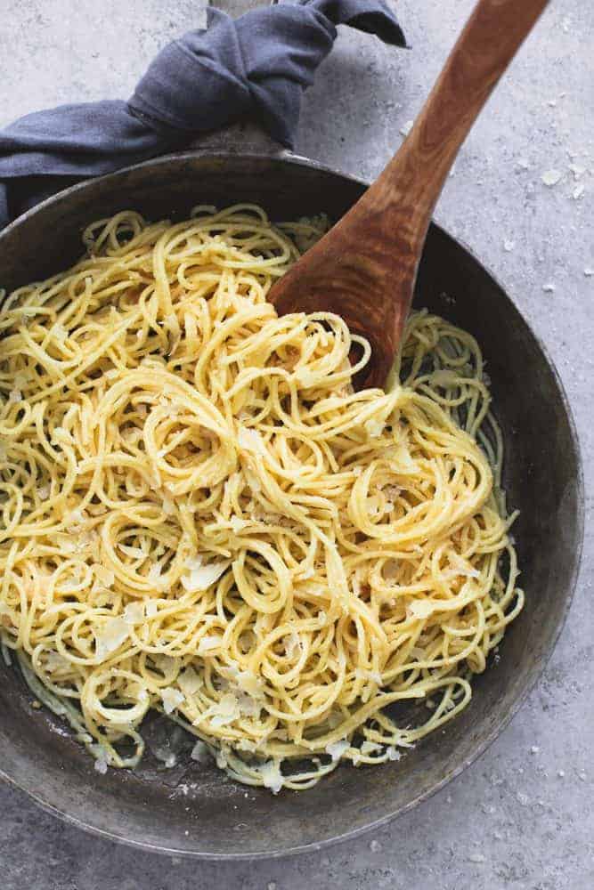 Creamy Parmesan spaghetti and a black skillet with the wooden spoon stirring. 