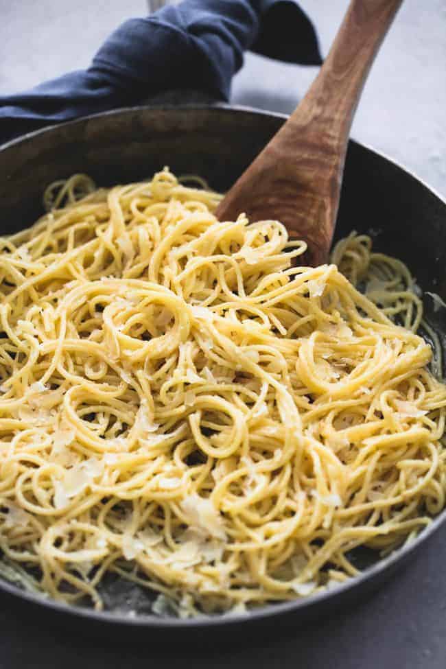 Creamy Parmesan Spaghetti in a black skillet with a wooden spoon stirring it.