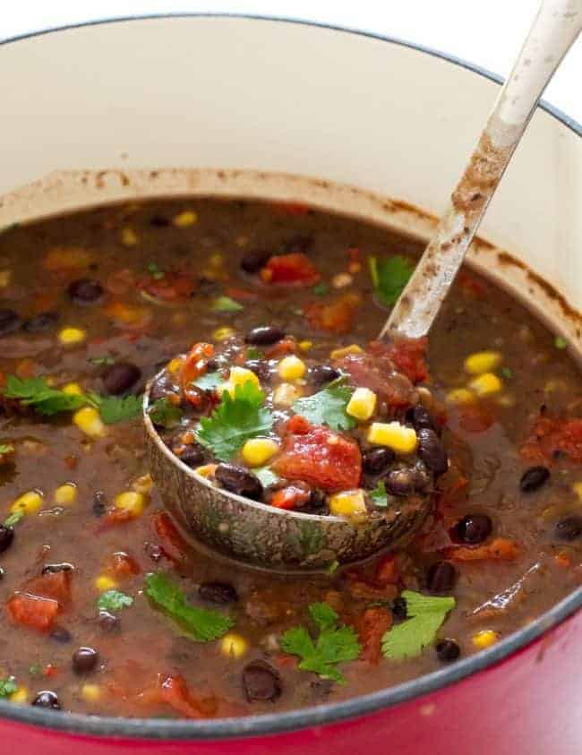 Black beans soup in a stew pot with a ladle scooping up soup. 