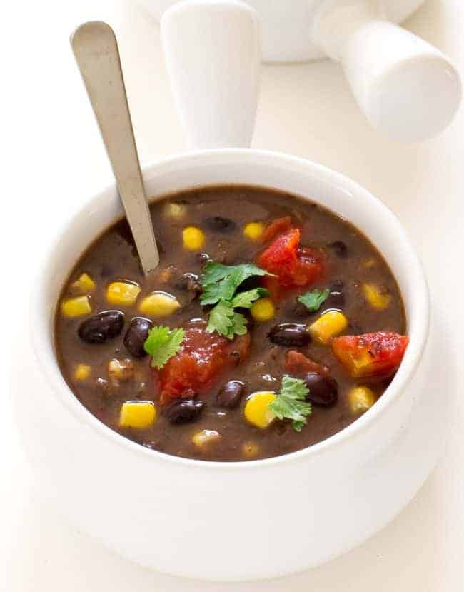 Black bean soup and a white bowl with a spoon in the soup. 