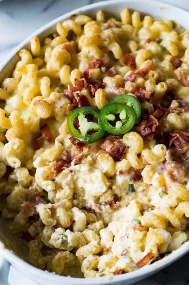 Jalapeño popper macaroni and cheese and a white casserole dish garnished with jalapeños and bacon bits.