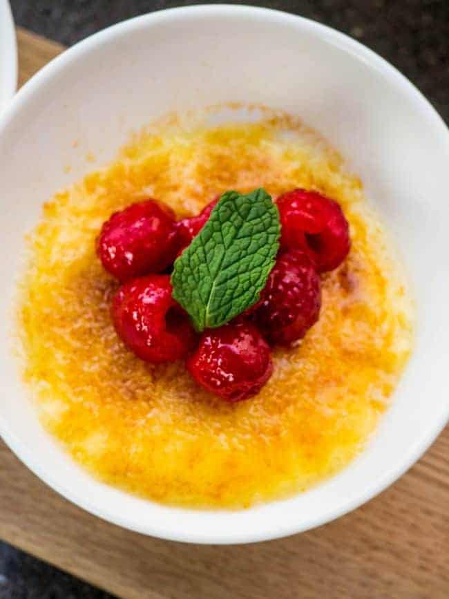 Cream Brûlée dessert garnished with raspberries on top and a mint leaf. 