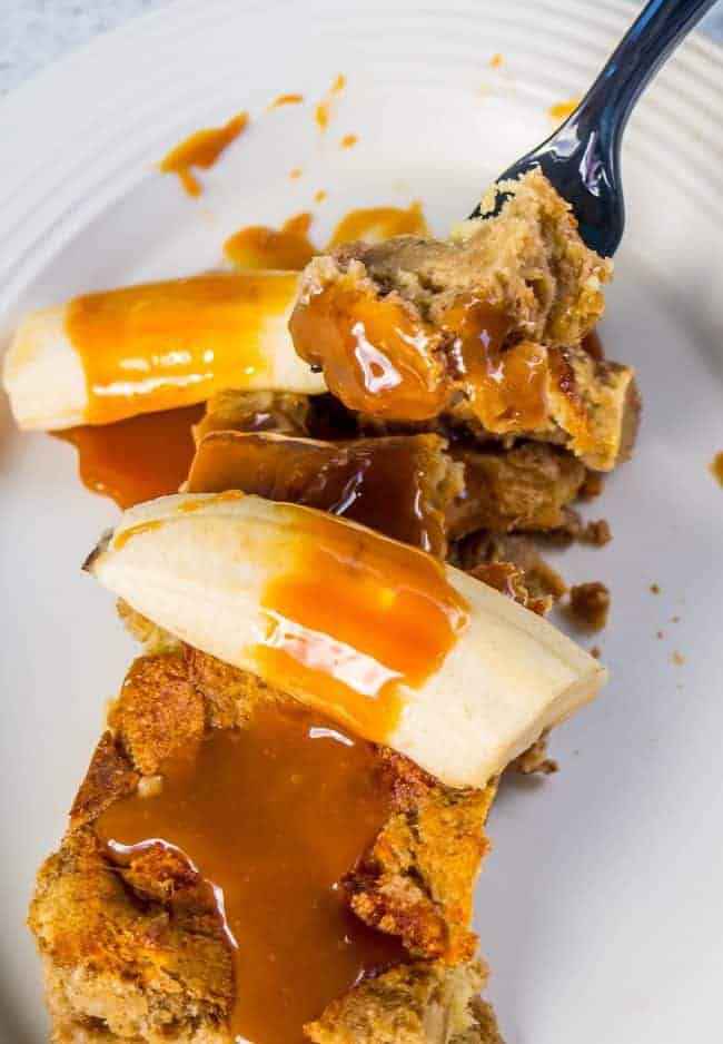 Overnight Caramel banana French toast with caramel syrup on a white plate with a fork in it.