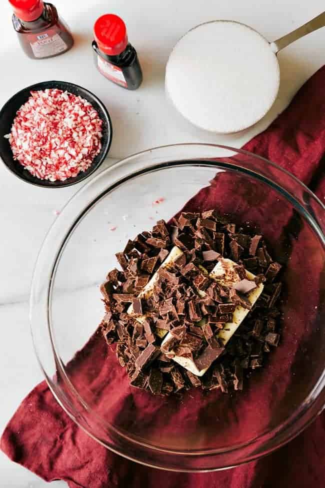 Chocolate chunks over top of sticks of butter with sprinkles in a glass bowl on the side a cuppa sugar and McCormick extracts on the side. 