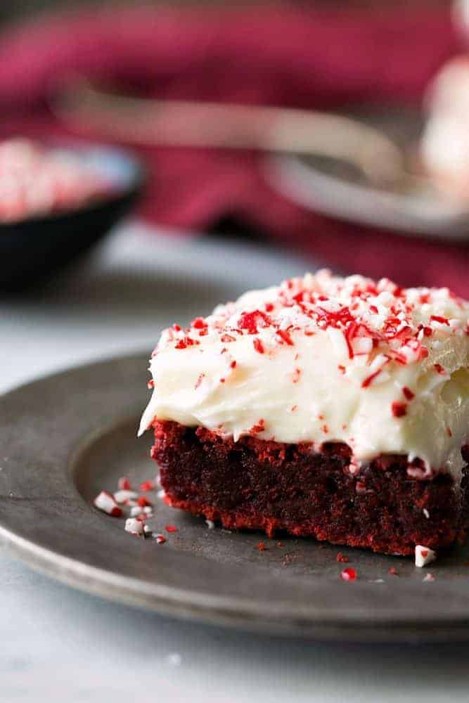 A slice of red velvet peppermint brownie with peppermint cream cheese frosting is on a gray plate.