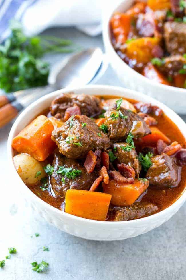 Beef stew with bacon and a white bowl.