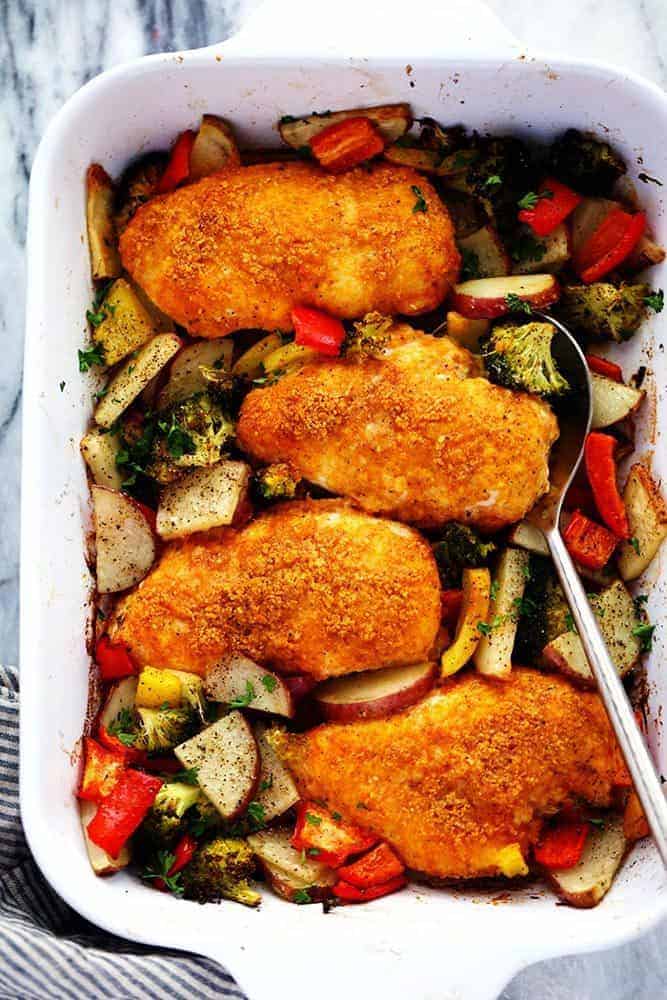 Crispy Parmesan Paprika Chicken with Vegetables in a casserole dish with a spoon on the side.