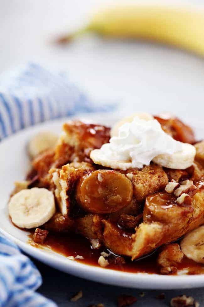Overnight Caramel banana French toast with caramel syrup on a white plate with whip topping as garnish. 
