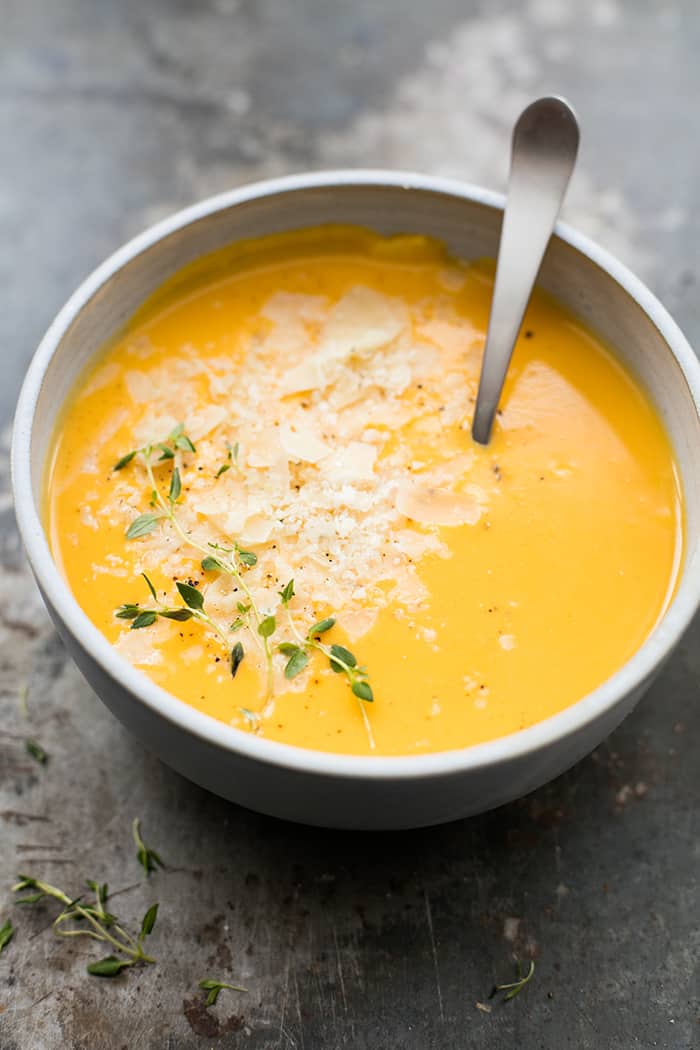 Butternut squash soup in a white bowl with a spoon in it garnished with cheese on top.