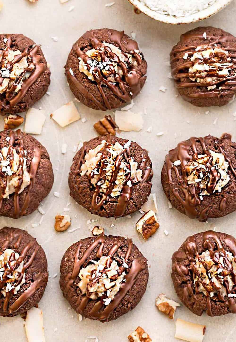German chocolate thumbprint cookies on a parchment paper with shreds of coconut and chopped walnuts. 