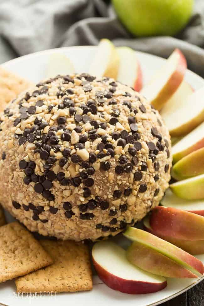 Snickers Cheese Ball and the middle of a serving tray with apple slices around it and wheat thin's on the other side.