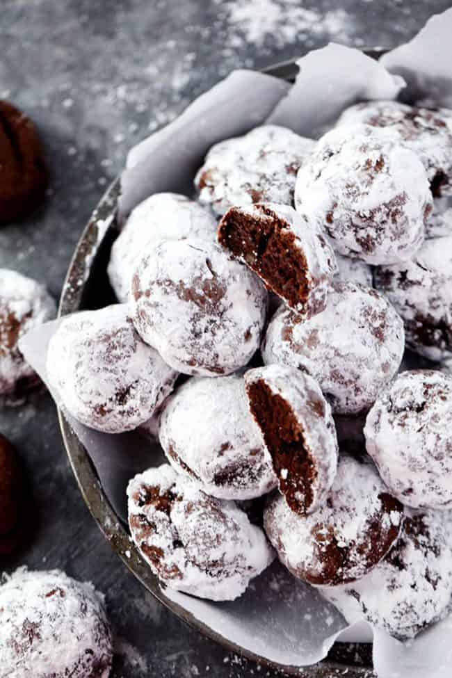 Chocolate Snowball cookies stacked on top of each other on parchment paper and a black bowl