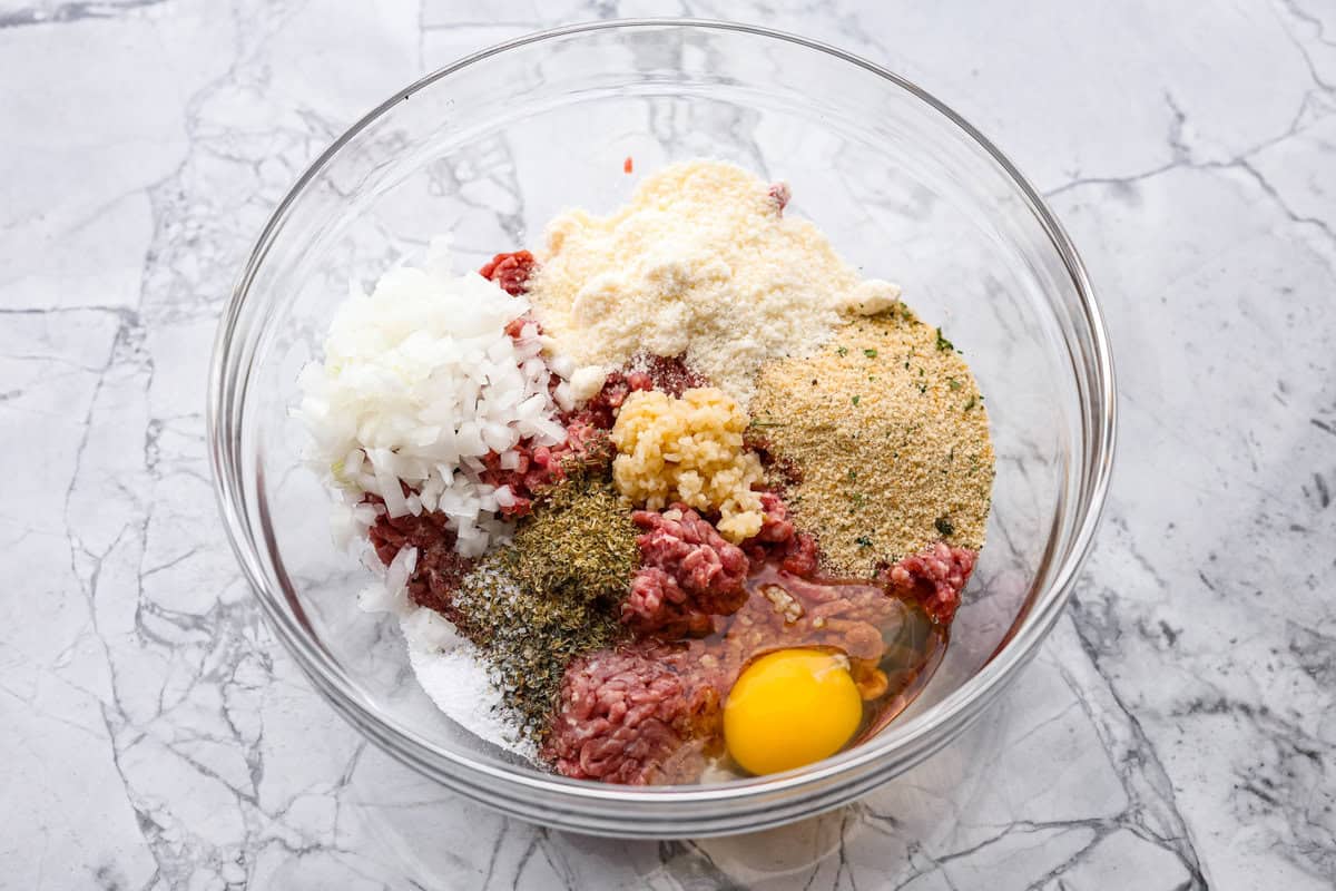 Mozzarella Stuffed Meatballs take classic meatballs to the next level! Tender and juicy with melty cheese on the inside. Serve these meatballs as a party appetizer or over spaghetti noodles for a hearty meal! First photo of meatball ingredients added to a bowl.