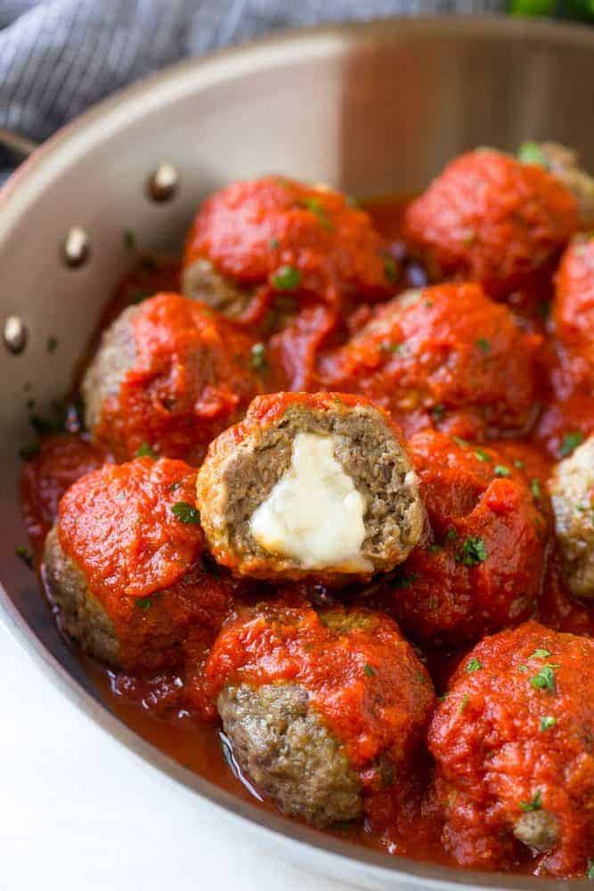 Mozzarella Stuffed Meatballs in a skillet. One of the meatballs has a bite taken out of it so you can see the mozzarella cheese flowing out of it.
