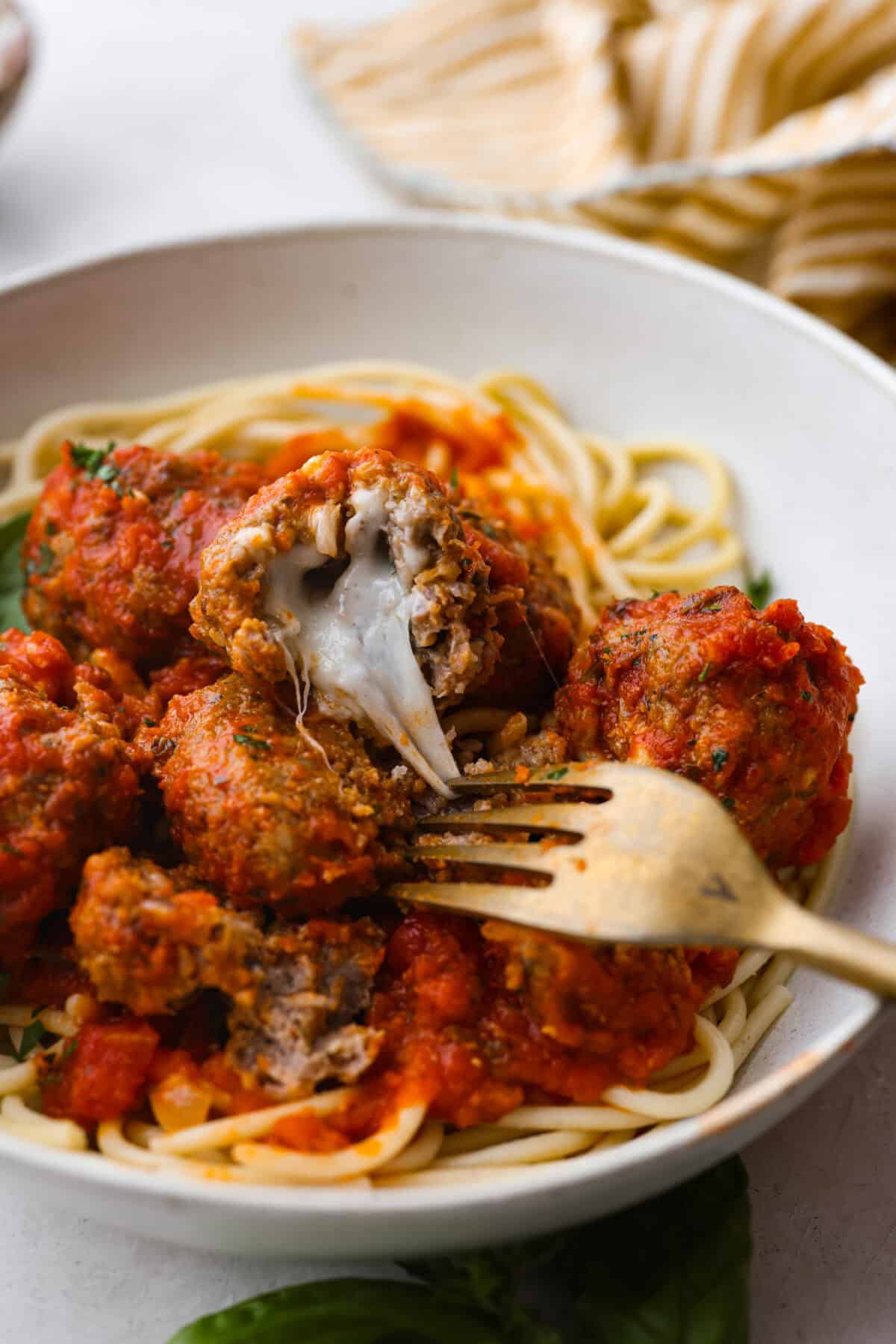 Close view of a fork pulling the melty cheese from a mozzarella stuffed meatball in a bowl.